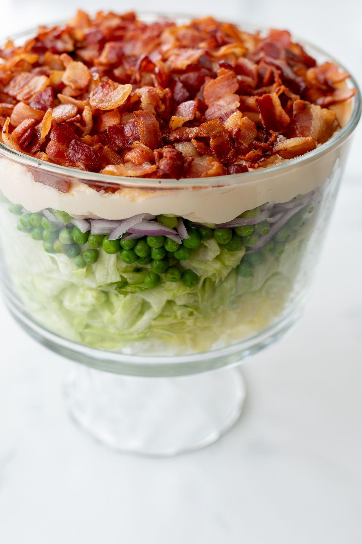 Siebenschichtsalat 2 Sieben-Schicht-Salat mit Speck belegt auf einer Marmorarbeitsplatte