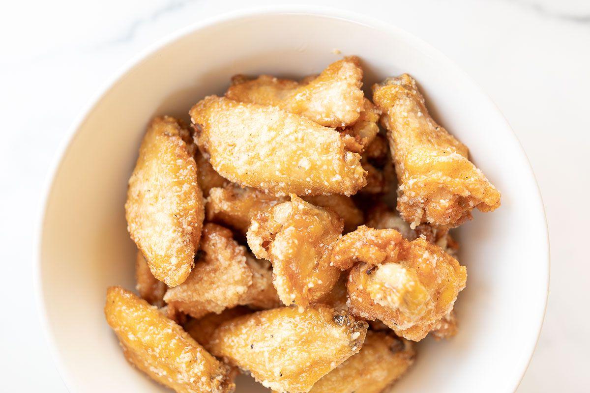 Knoblauch-Parmesan-Hähnchenflügel 2 Eine weiße Schale gefüllt mit goldenen Knoblauch-Parmesan-Hähnchenflügeln auf einer glänzenden Marmorarbeitsplatte