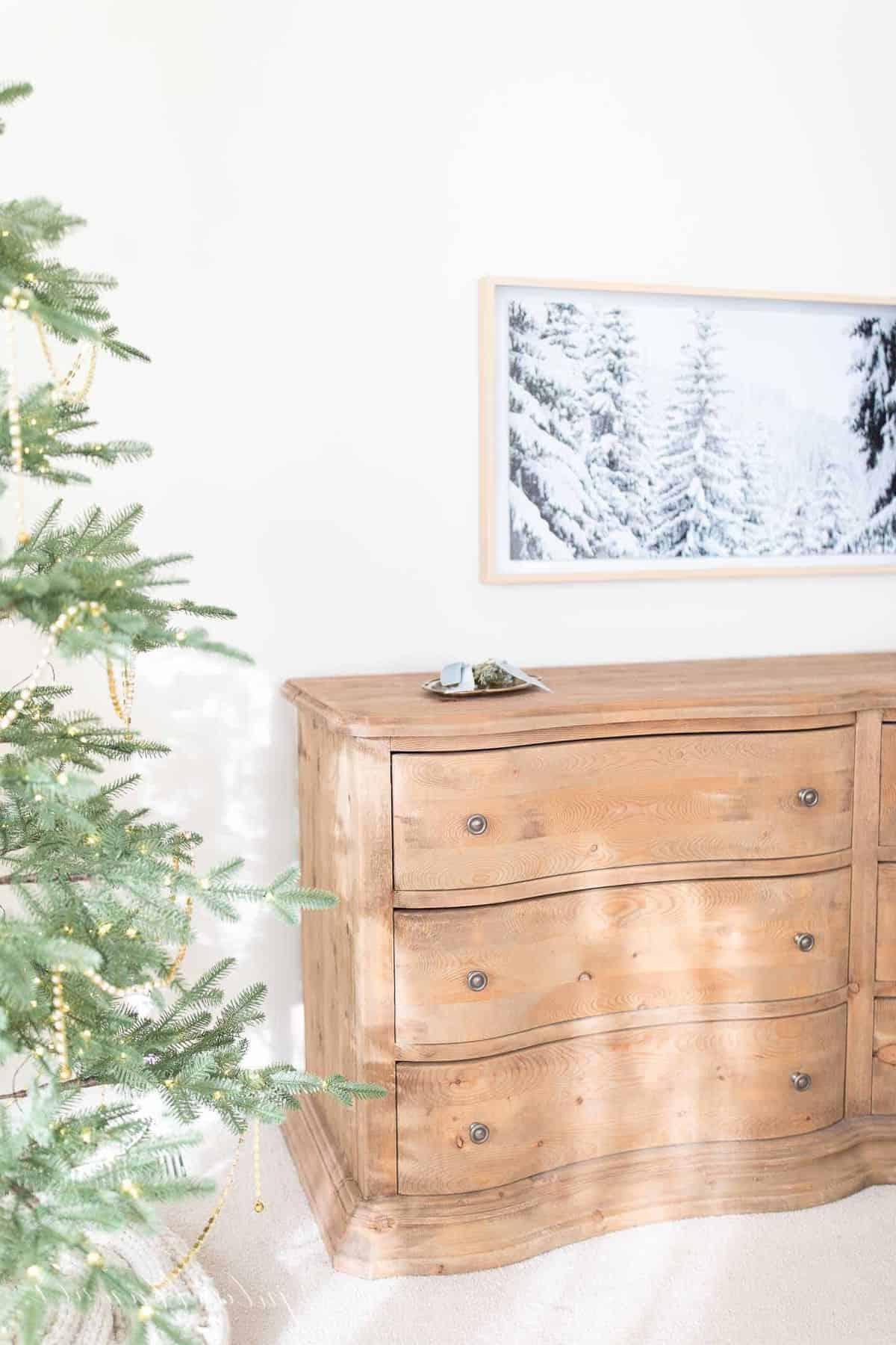 **Wo man Kunst für den Samsung The Frame TV kaufen kann** 2 Ein Samsung Art TV an der Wand eines Schlafzimmers, der eine Winterlandschaft zeigt, mit einem Weihnachtsbaum im Vordergrund.