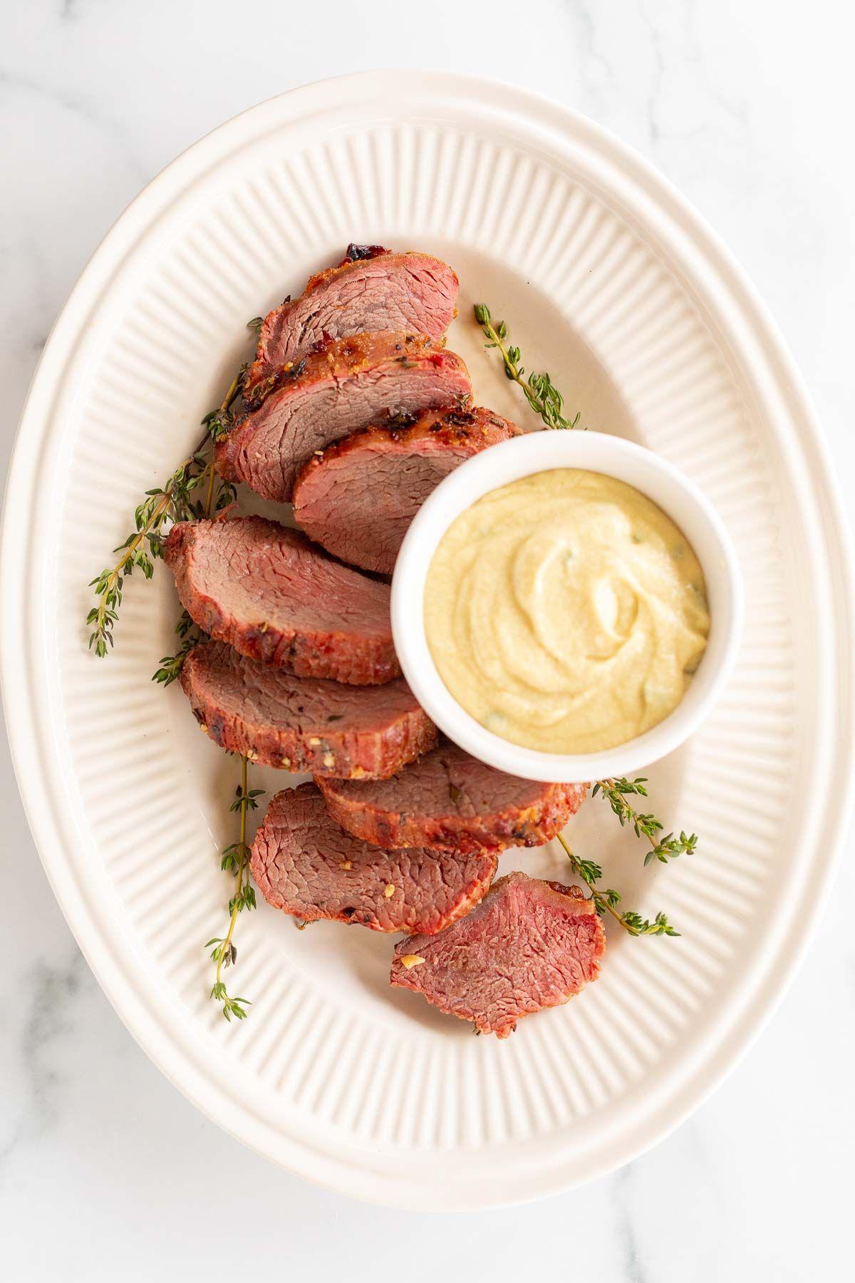 Eine weiße Schale voller Dijon-Senfsauce, umgeben von Rinderfilet auf einer Platte