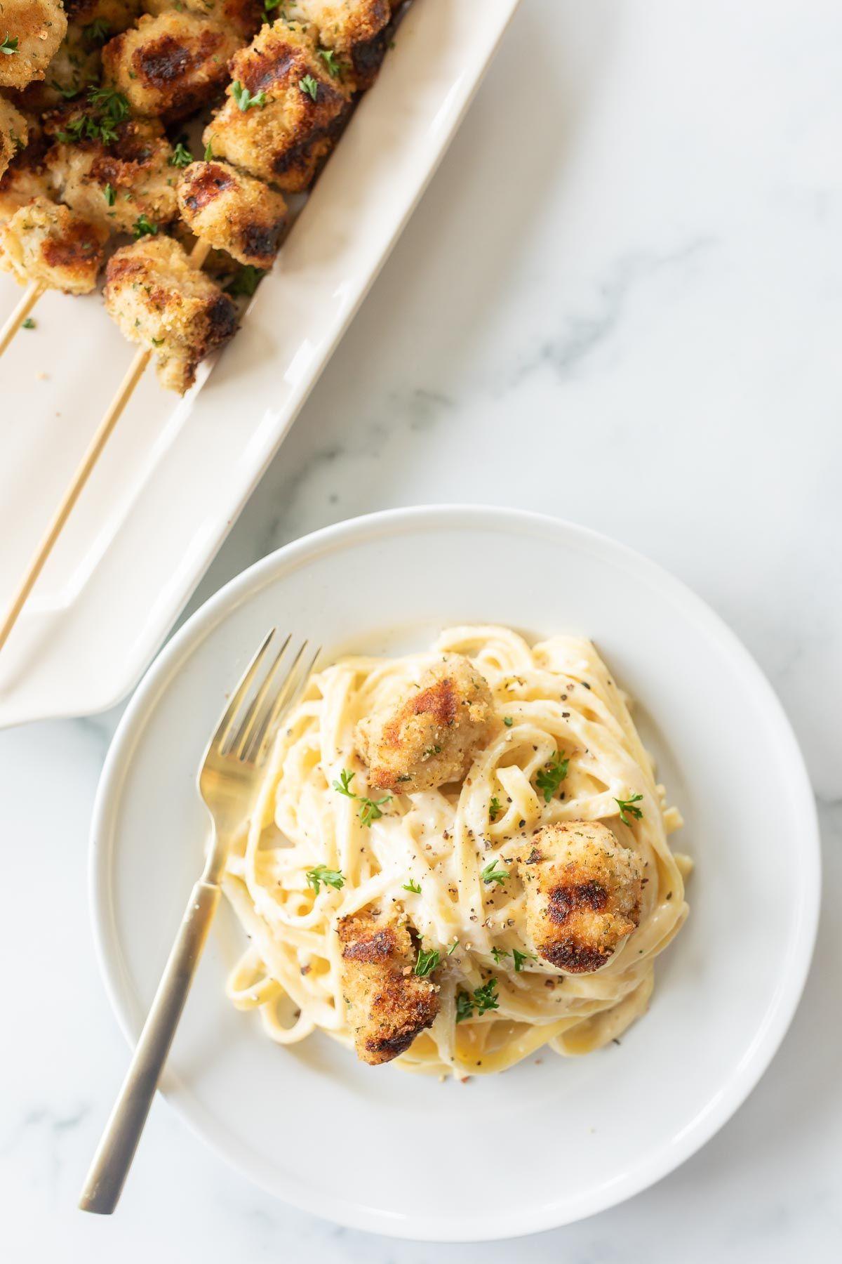 Spießchen 2 Fettuccine Alfredo mit Spiedini auf einem weißen Teller, im Hintergrund eine Platte mit Hähnchen Spiedini.