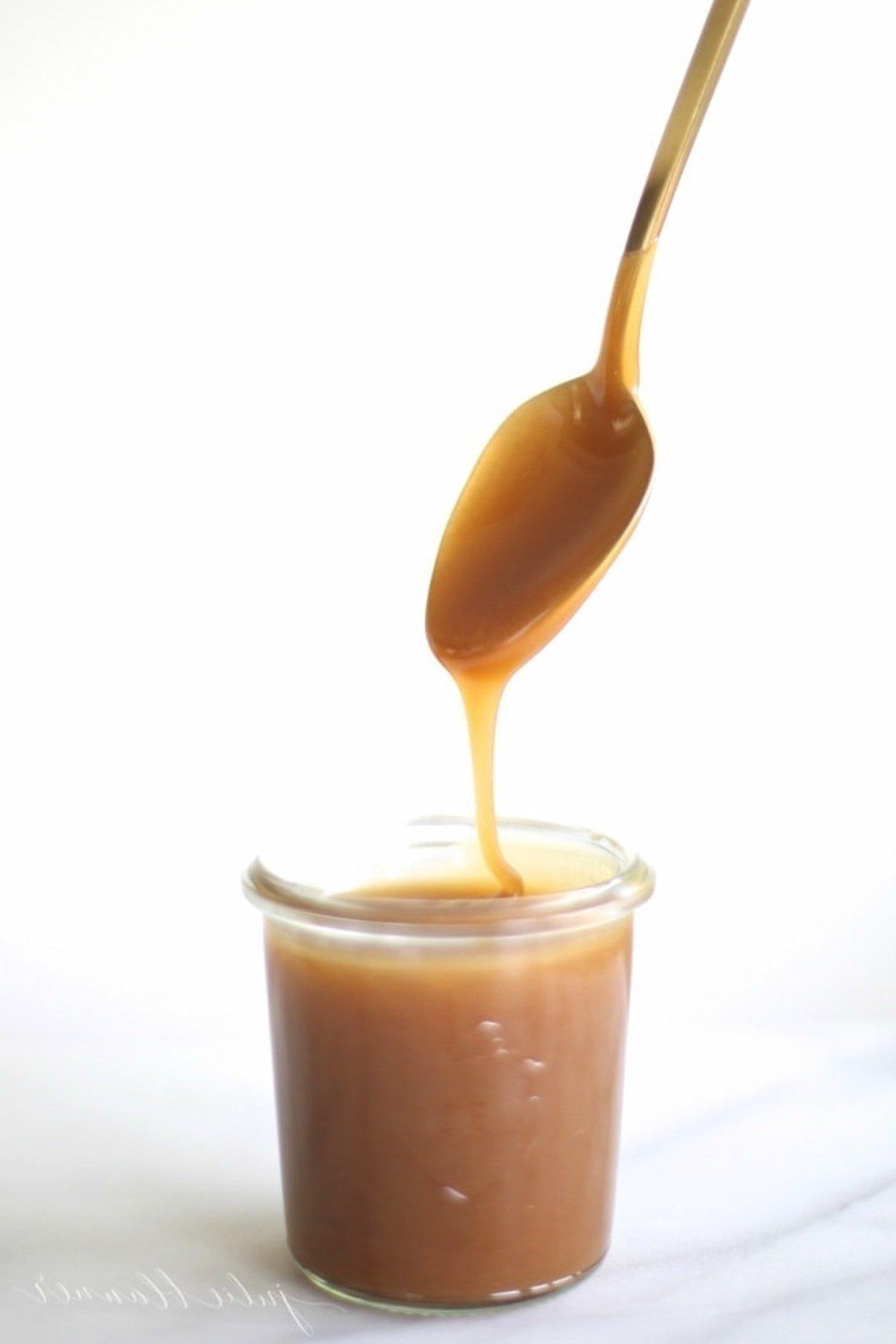 Gesalzene Karamellsoße 2 Ein Löffel gießt Karamellsauce, insbesondere gesalzene Karamellsauce, in ein Glas.