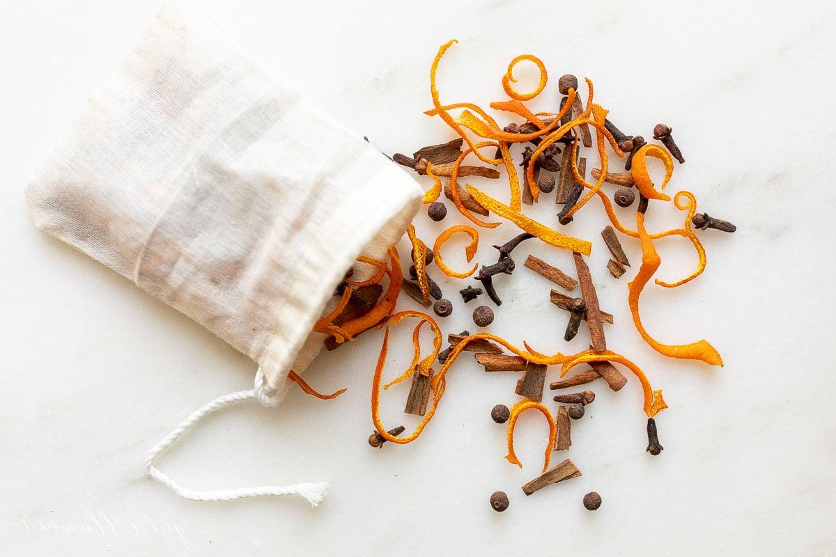 Glühweingewürz Rezept für Glühwein, gewürzten Apfelpunsch oder duftendes Potpourri, mit einer Mischung aus Zimtstangen, Piment, ganzen Nelken und Orangenschalen. Ein Teebeutel gefüllt mit Glühweingewürz, bereit zum Aufbrühen in einem Becher.