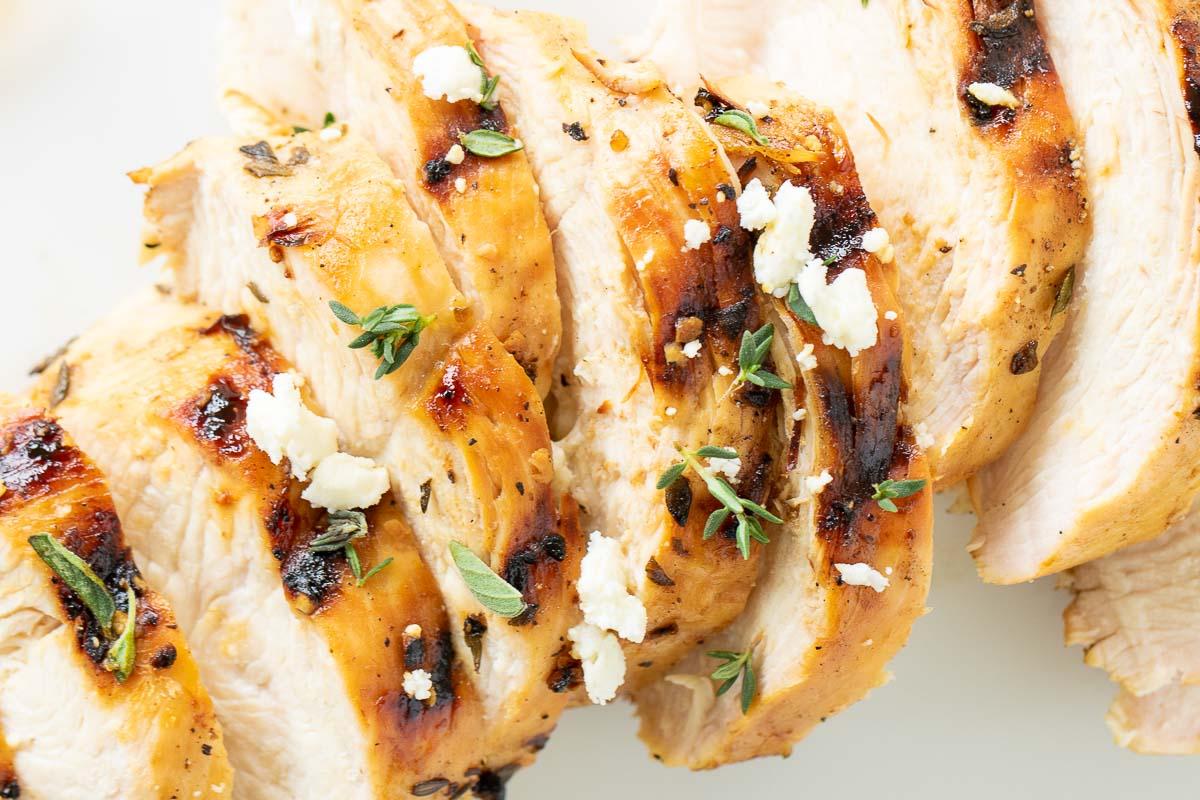 Griechisches Hähnchen 2 Auf einer weißen Oberfläche liegen Scheiben von griechisch mariniertem Hähnchen, daneben gegrillte Zitrone.