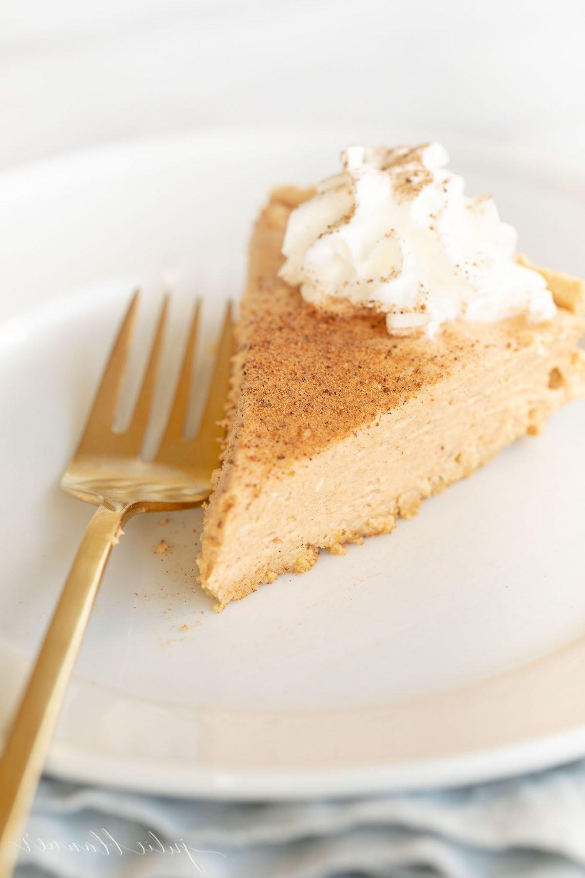 Einfaches Kürbis-Käsekuchen-Rezept ohne Backen 2 Kürbis-Käsekuchen mit Schlagsahne gekrönt auf einem weißen Teller, daneben eine goldene Gabel.