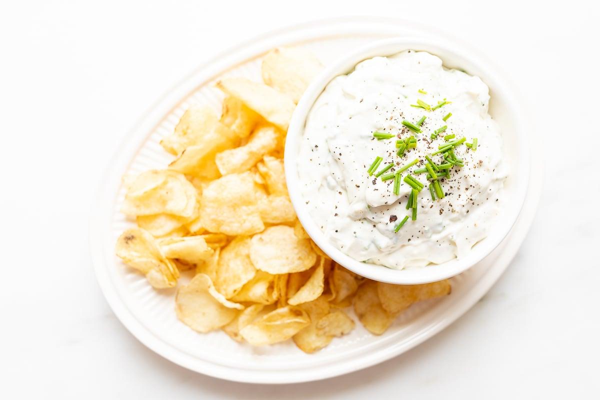 Ein cremiger Blauschimmelkäse-Dip in einer eleganten weißen Schale, appetitlich auf einer Platte mit knusprigen Kartoffelchips arrangiert.