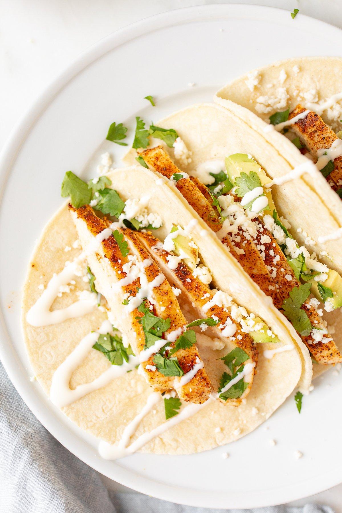 Weiche Hähnchen-Tacos 2 Mais-Tortillas in einer Reihe mit Hähnchen-Tacos auf einem weißen Tisch.