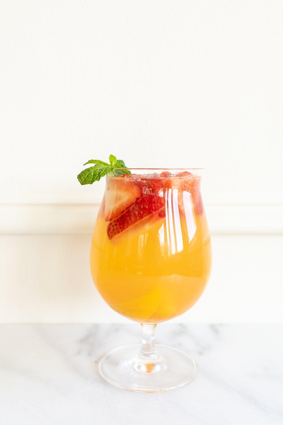 Ein Glas Moscato Sangria, garniert mit Erdbeeren, Pfirsichen und Minze.