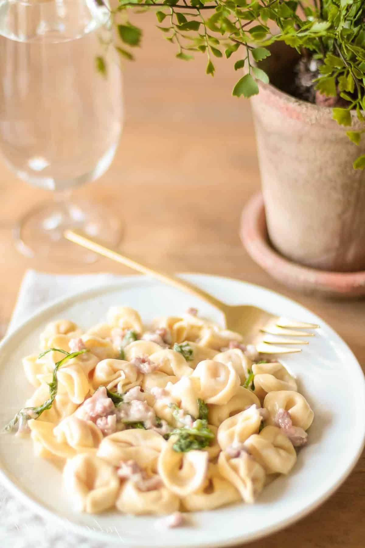 Tortellacci mit Prosciutto, Rucola und Trüffelöl auf einem Teller mit einer goldenen Gabel und einem Glas daneben