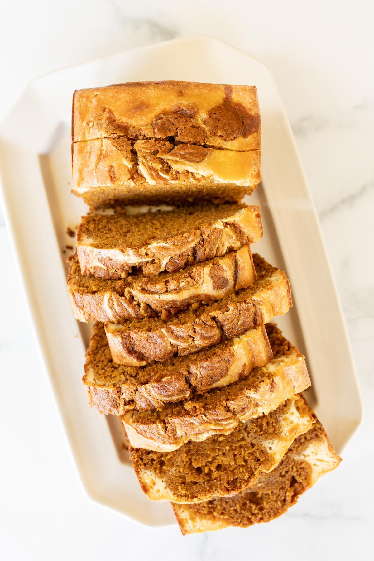 Ein ganzer Laib Kürbis-Käsekuchen-Brot auf einer weißen Servierplatte, fertig zum Anschneiden.