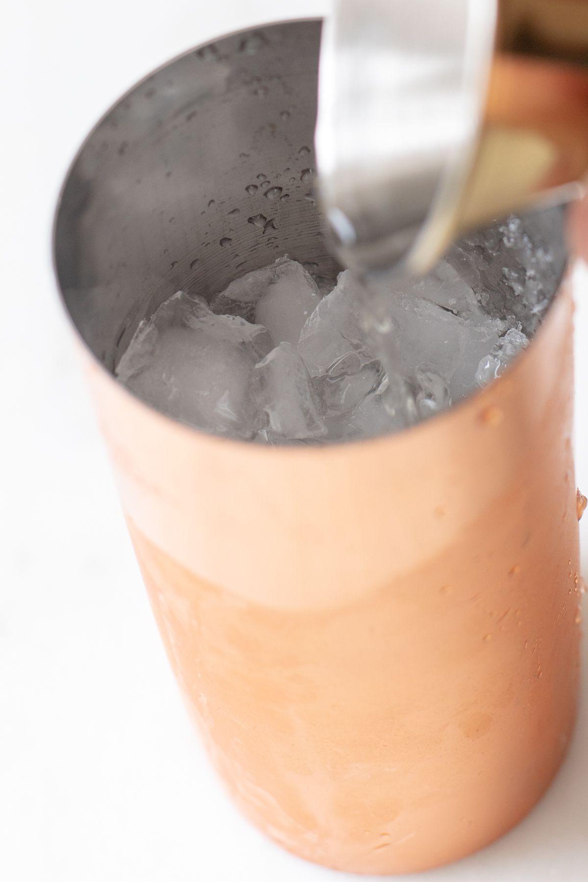 Ein kupferfarbener Shaker mit einer Hand, die Cadillac Margarita Zutaten mixt.