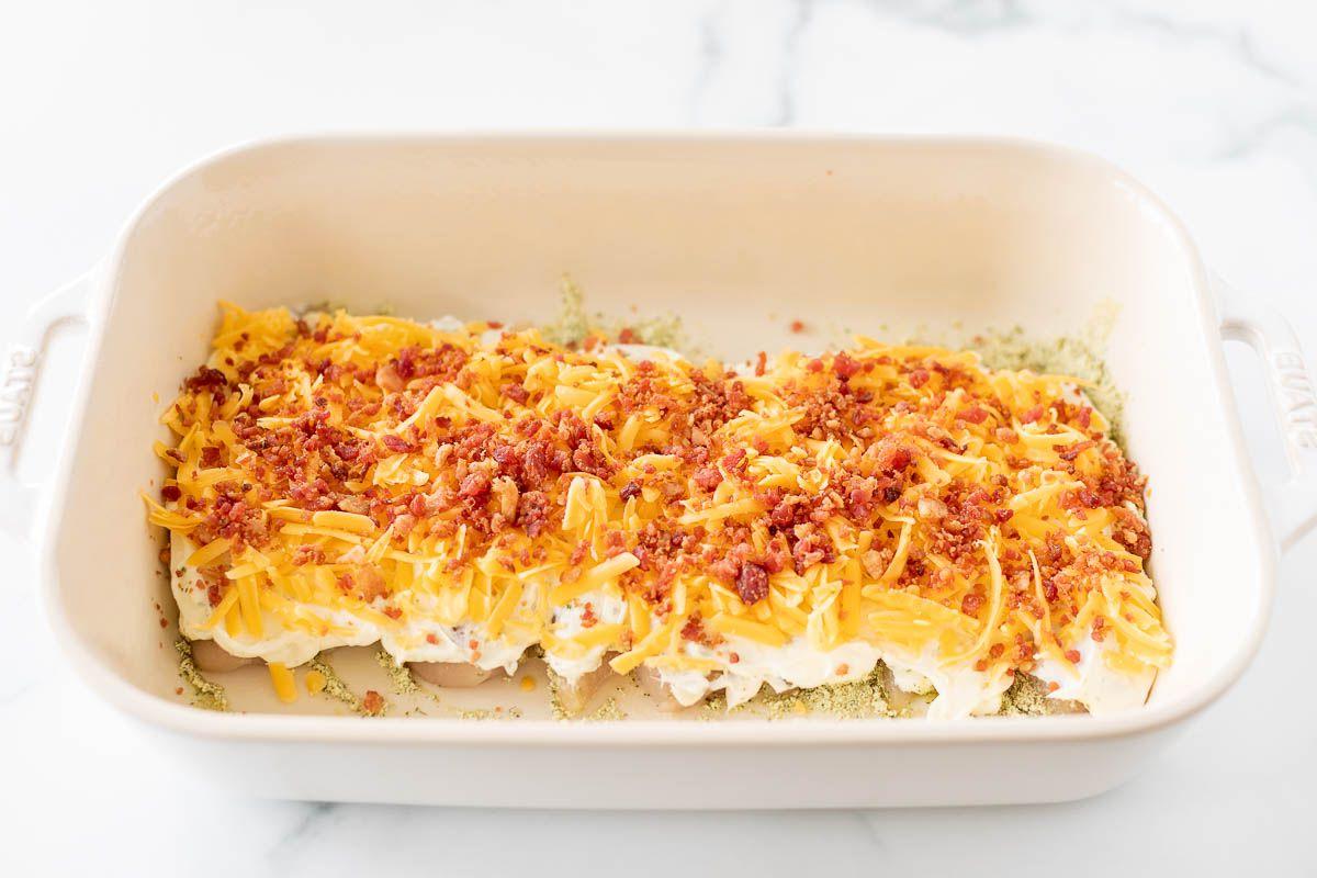 Eine weiße Auflaufform mit cremigem, käsigen 'Crack Chicken', garniert mit Frühlingszwiebeln und gehacktem Speck.