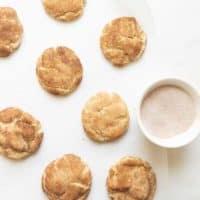 Die besten weichen Snickerdoodles 11 Weiche und fluffige Snickerdoodle-Kekse auf einer weißen Arbeitsplatte mit einer Schüssel Zimt und Zucker. #easysnickerdoodlecookierecipe #softsnickerdoodlerecipe