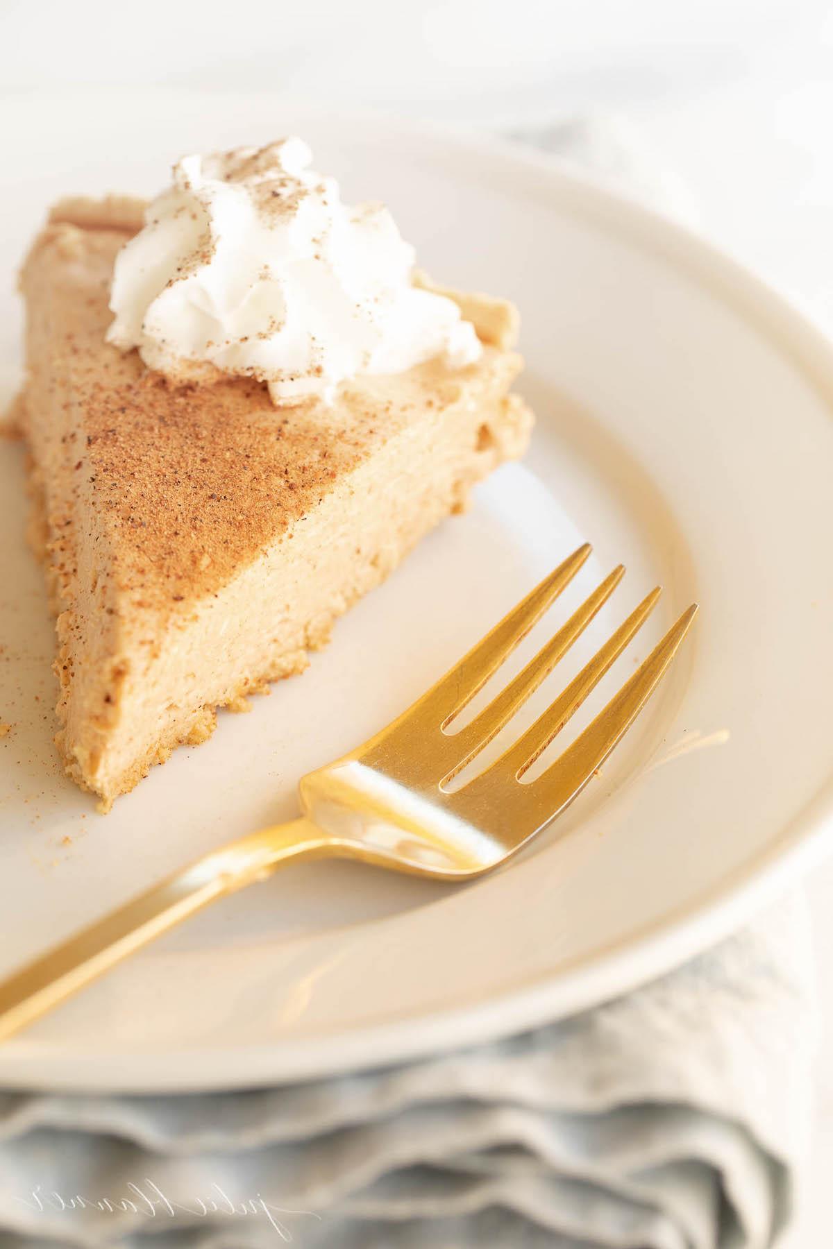 Einfaches Kürbis-Käsekuchen-Rezept ohne Backen 10 Kürbis-Käsekuchen mit Schlagsahne gekrönt auf einem weißen Teller, daneben eine goldene Gabel.