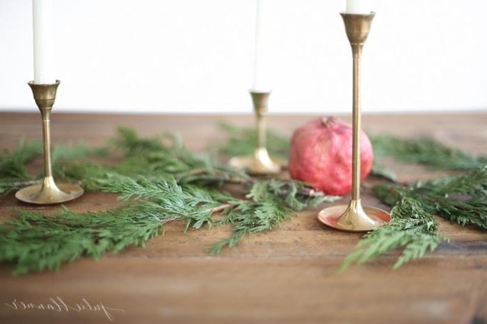 Ein atemberaubendes Weihnachts-Kerzen-Mittelstück mit drei Messingkerzenständern, geschmückt mit Grünzeug und einem Granatapfel.