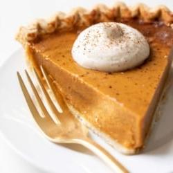 Eierpunschschlagsahne 12 Ein Stück Kürbiskuchen mit einem Klecks Eierpunsch-Schlagsahne darauf, eine appetitliche Nahaufnahme des Desserts.