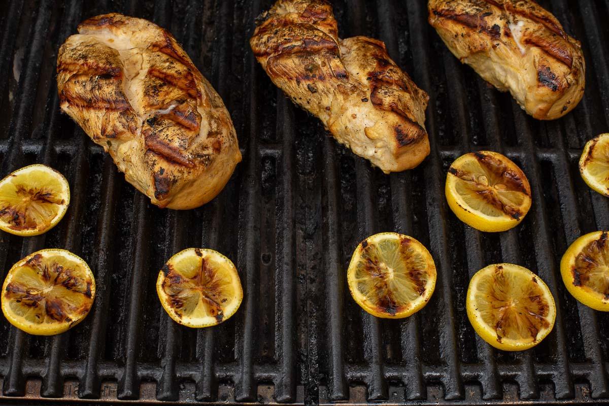 Gegrilltes griechisches Hähnchen und Zitronenscheiben auf einem Gasgrill.