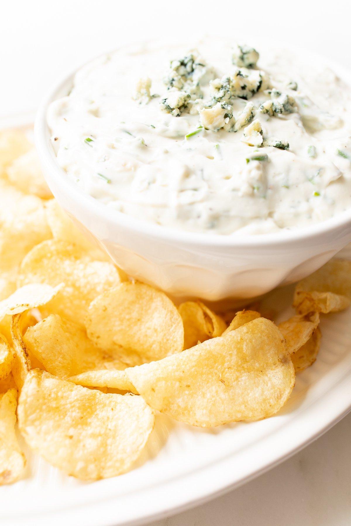 Ein appetitlicher Blauschimmelkäse-Dip in einer weißen Schale, umgeben von knusprigen Kartoffelchips auf einer Servierplatte, bereit zum Genießen.