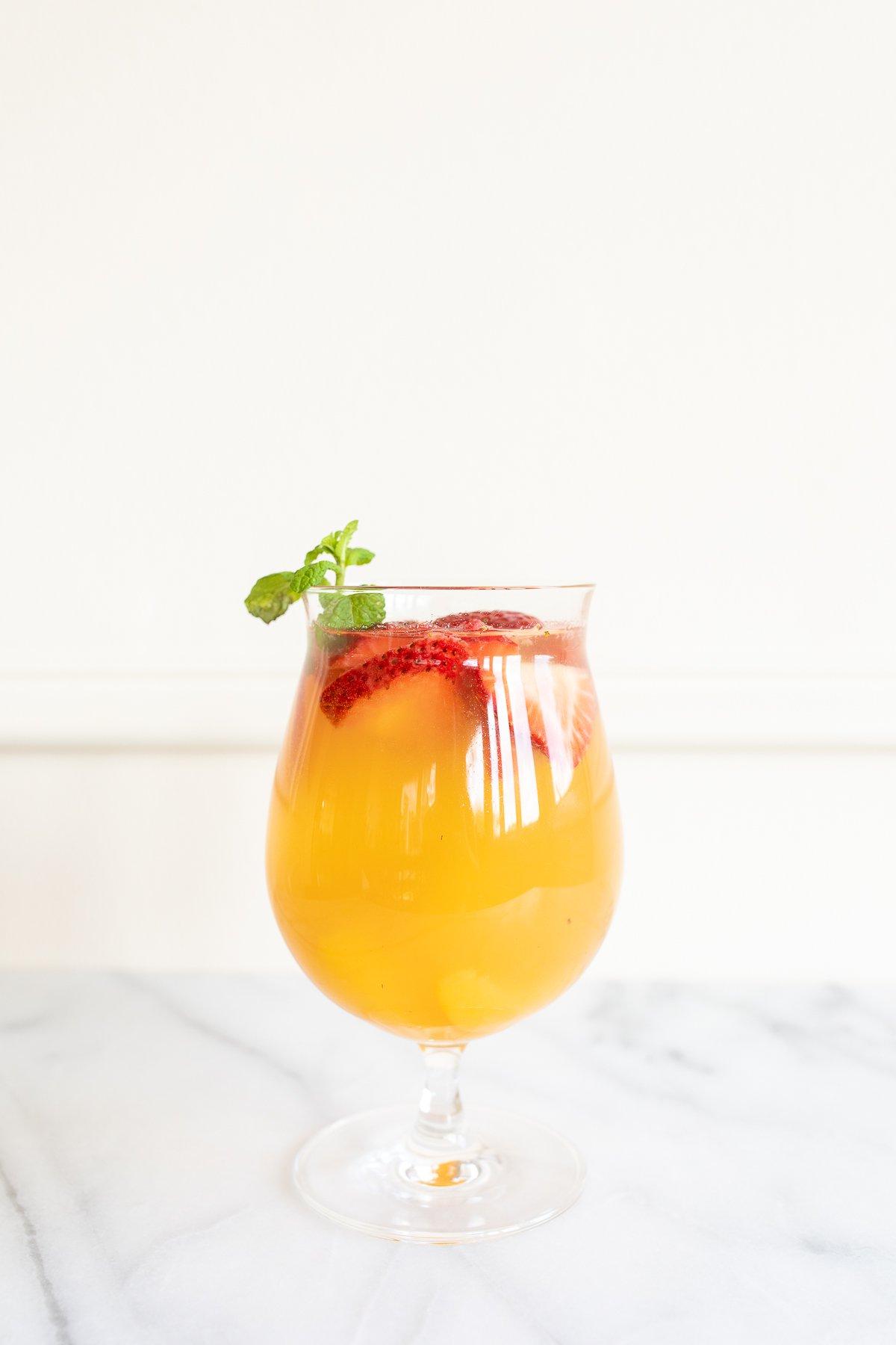 Ein Glas Moscato Sangria, garniert mit Erdbeeren, Pfirsichen und Minze.