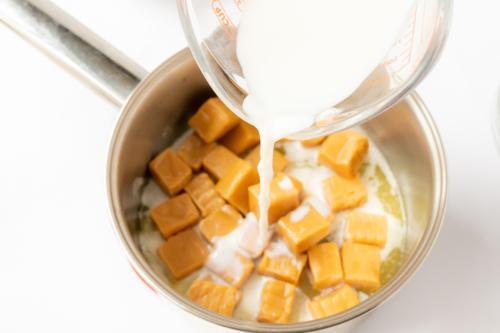 Karamellwürfel werden für ein köstliches Karamell-Pekannusskuchen-Rezept in einen Topf mit Milch gegeben, um eine glatte Mischung zu bilden.