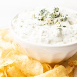 Ein appetitlicher Blauschimmelkäse-Dip in einer weißen Schale, umgeben von knusprigen Kartoffelchips auf einer Servierplatte, bereit zum Genießen.