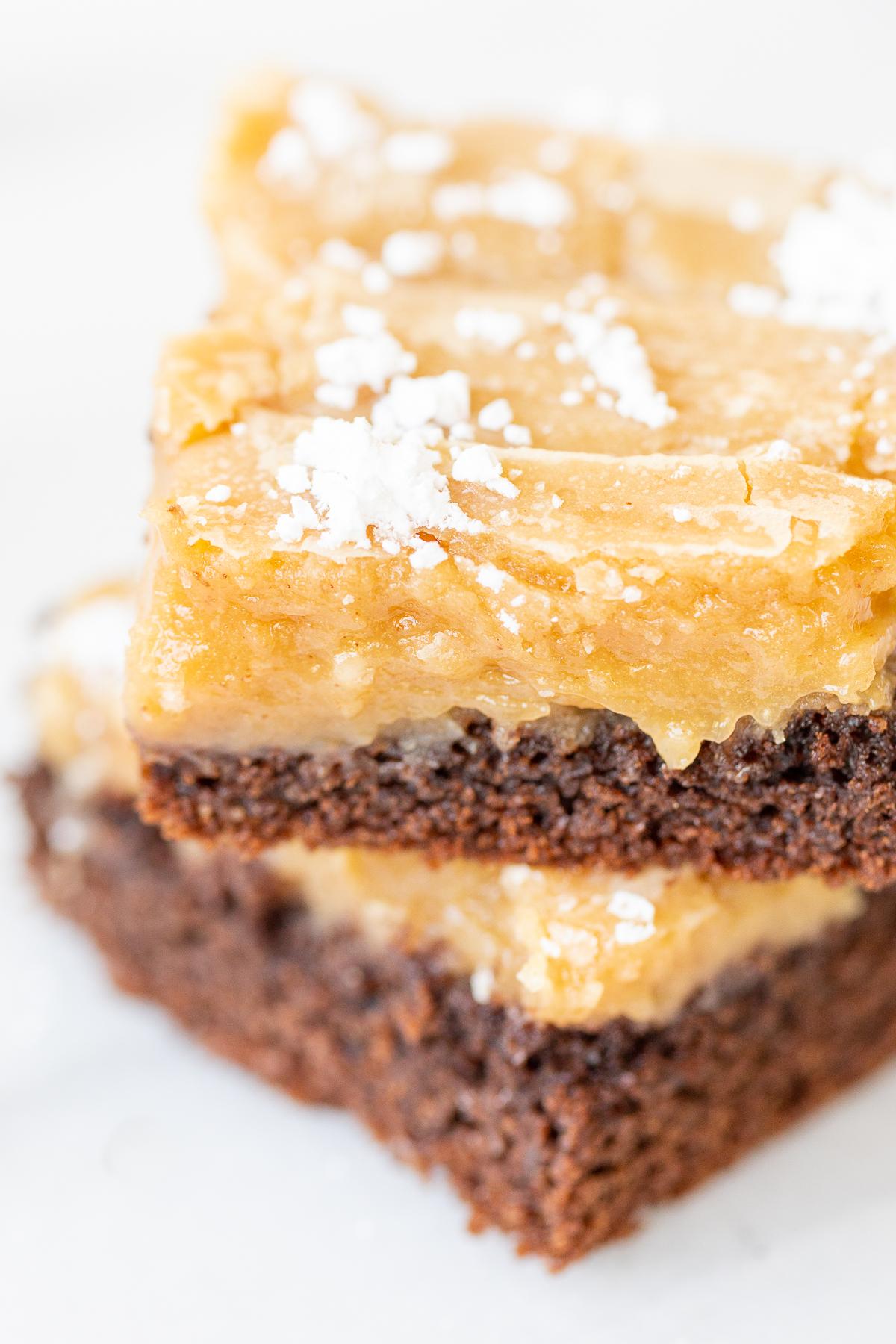 Zartschmelzender Erdnussbutter-Butterkuchen 13 Zwei Stücke Erdnussbutter Gooey Butter Kuchen, auf einer weißen Oberfläche gestapelt.
