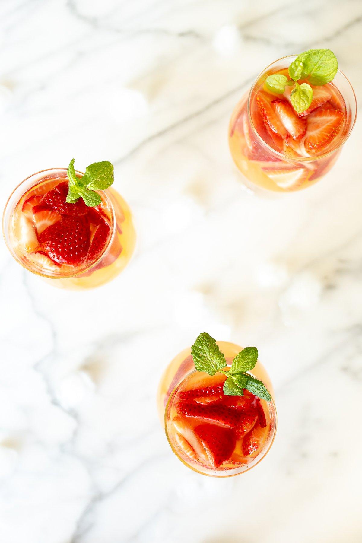 Drei Gläser Moscato Sangria, garniert mit Erdbeeren, Pfirsichen und Minze.