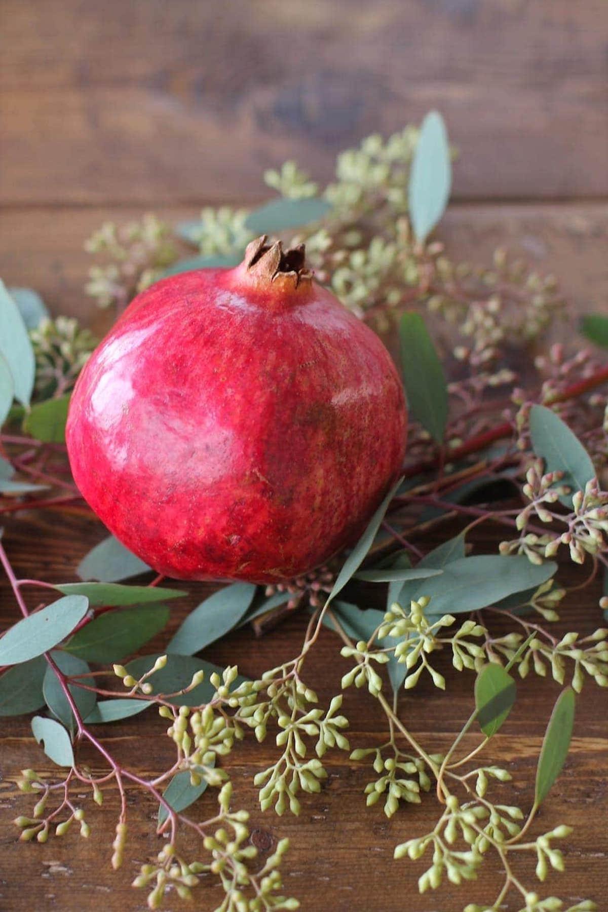 Weihnachts-Kerzen-Mittelstück mit Granatapfel und Eukalyptusblättern auf einem Holztisch.