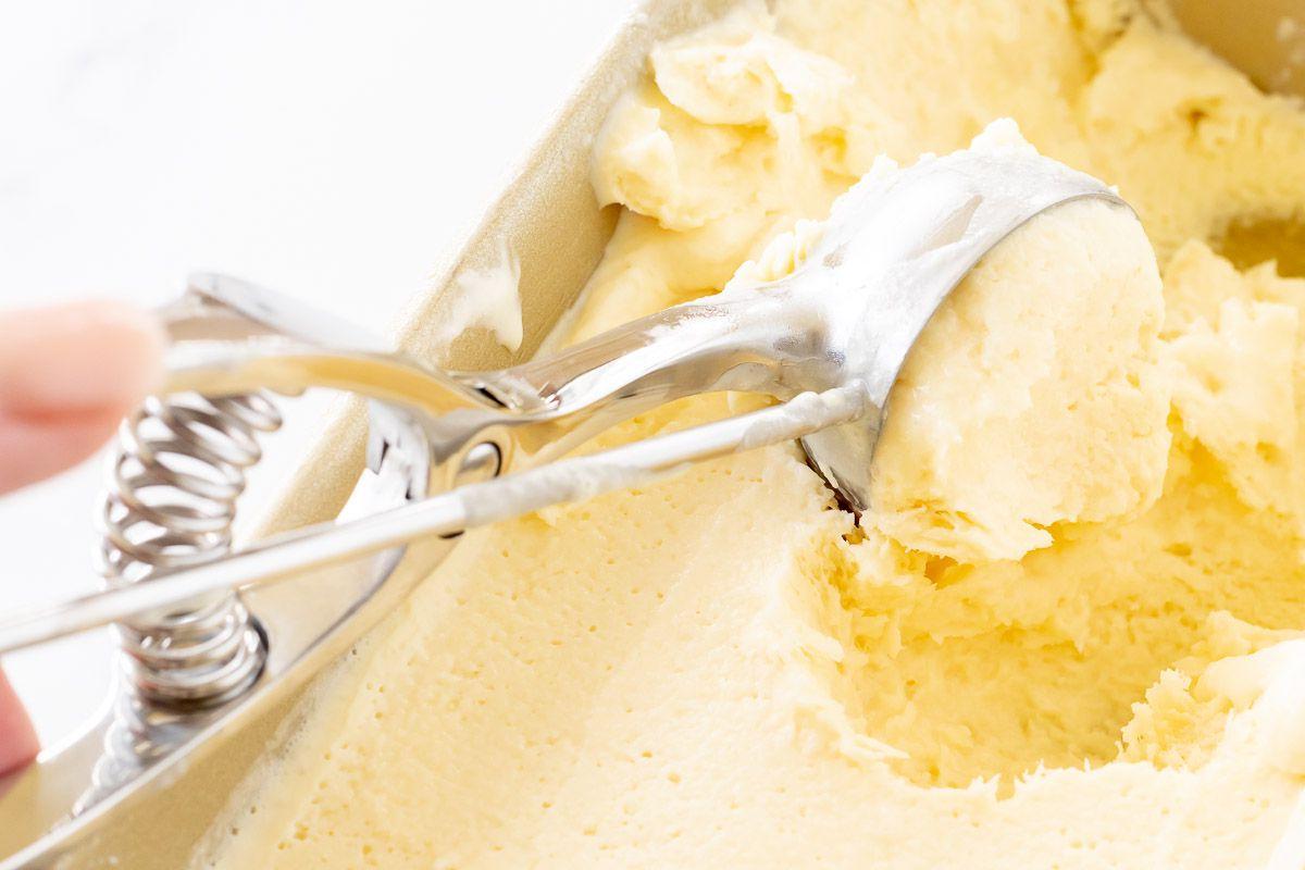Orangen-Sorbet 14 Nahaufnahme von hausgemachtem Orangen-Sherbet in einer goldenen Brotkastenform, mit einem Eisportionierer