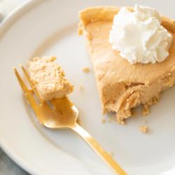 Einfaches Kürbis-Käsekuchen-Rezept ohne Backen 13 Kürbis-Käsekuchen mit Schlagsahne gekrönt auf einem weißen Teller, daneben eine goldene Gabel.