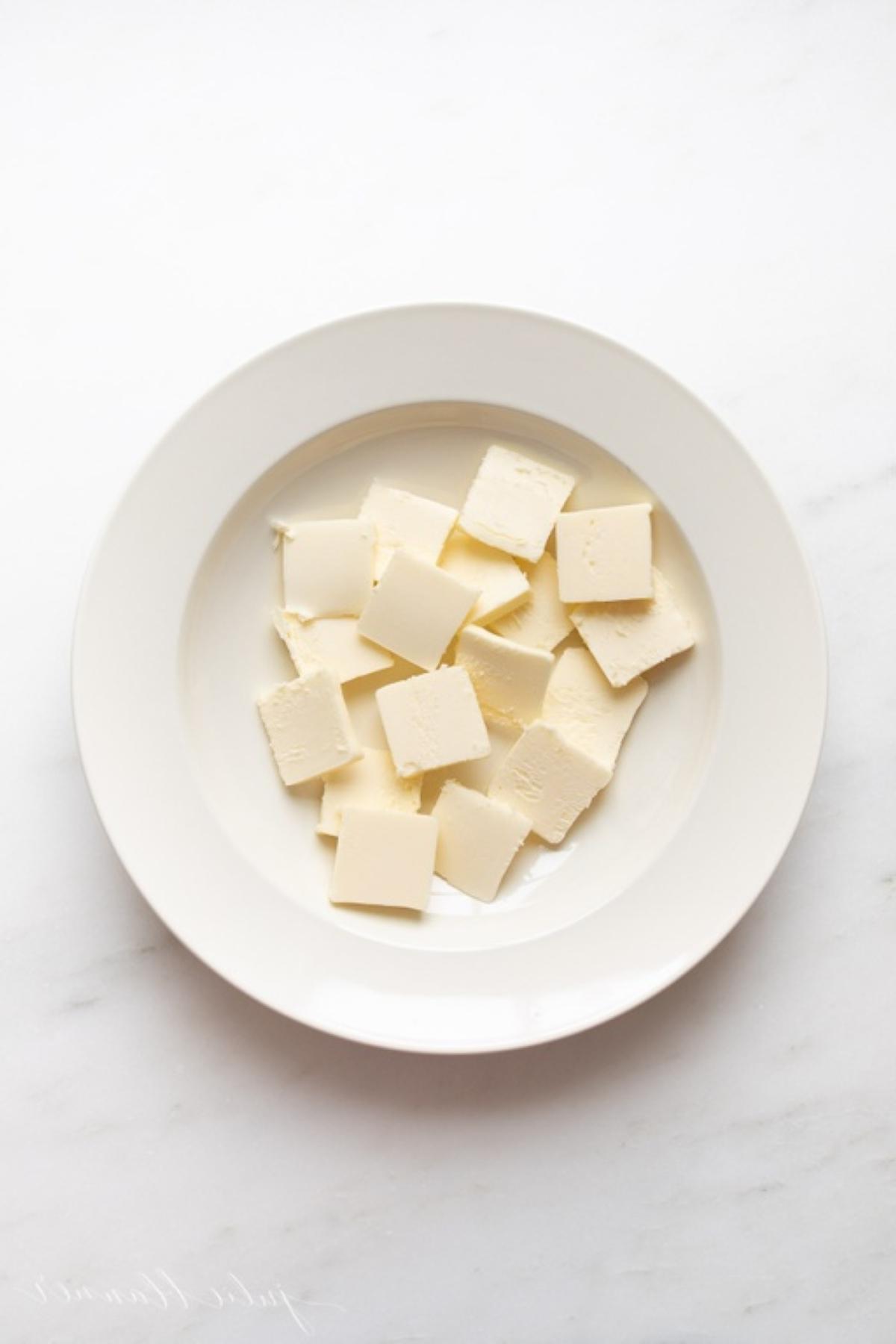 Ein weißer Teller voller Butterstücke in einem Tutorial zum schnellen Weichmachen von Butter.
