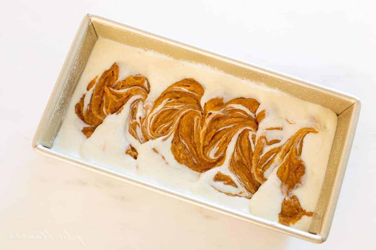Eine goldene Kastenform, gefüllt mit der Kürbisbrot-Masse und der Käsekuchenfüllung, bereit zum Backen.