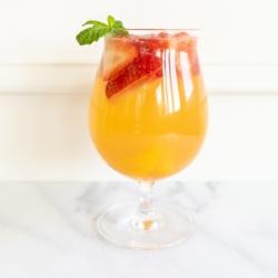 Ein Glas Moscato Sangria, garniert mit Erdbeeren, Pfirsichen und Minze.