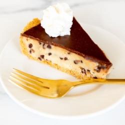 Keksteigkuchen 15 Ein weißer Teller mit einem Stück Keksteig-Kuchen und einer goldenen Gabel.