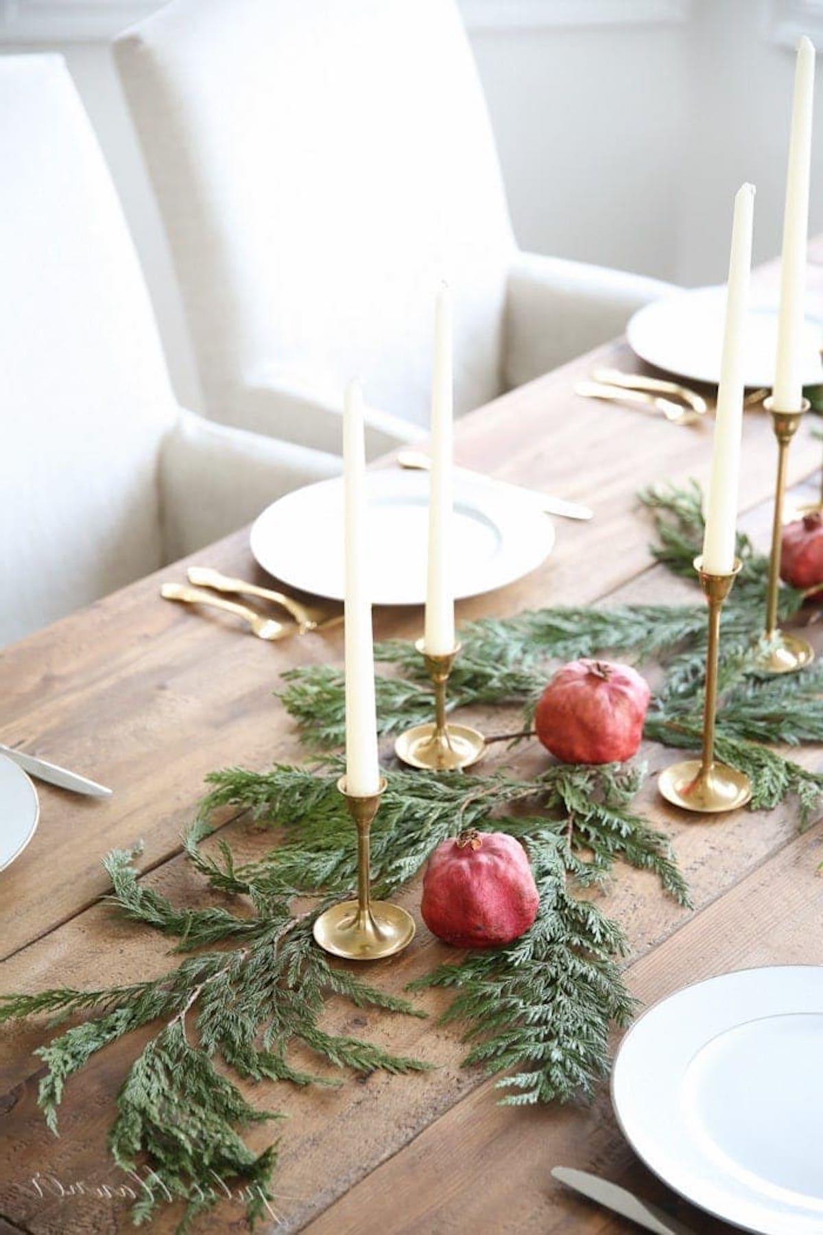 Ein festlich gedeckter Weihnachtstisch mit einem fesselnden Mittelstück-Arrangement aus Kerzen und Granatäpfeln.