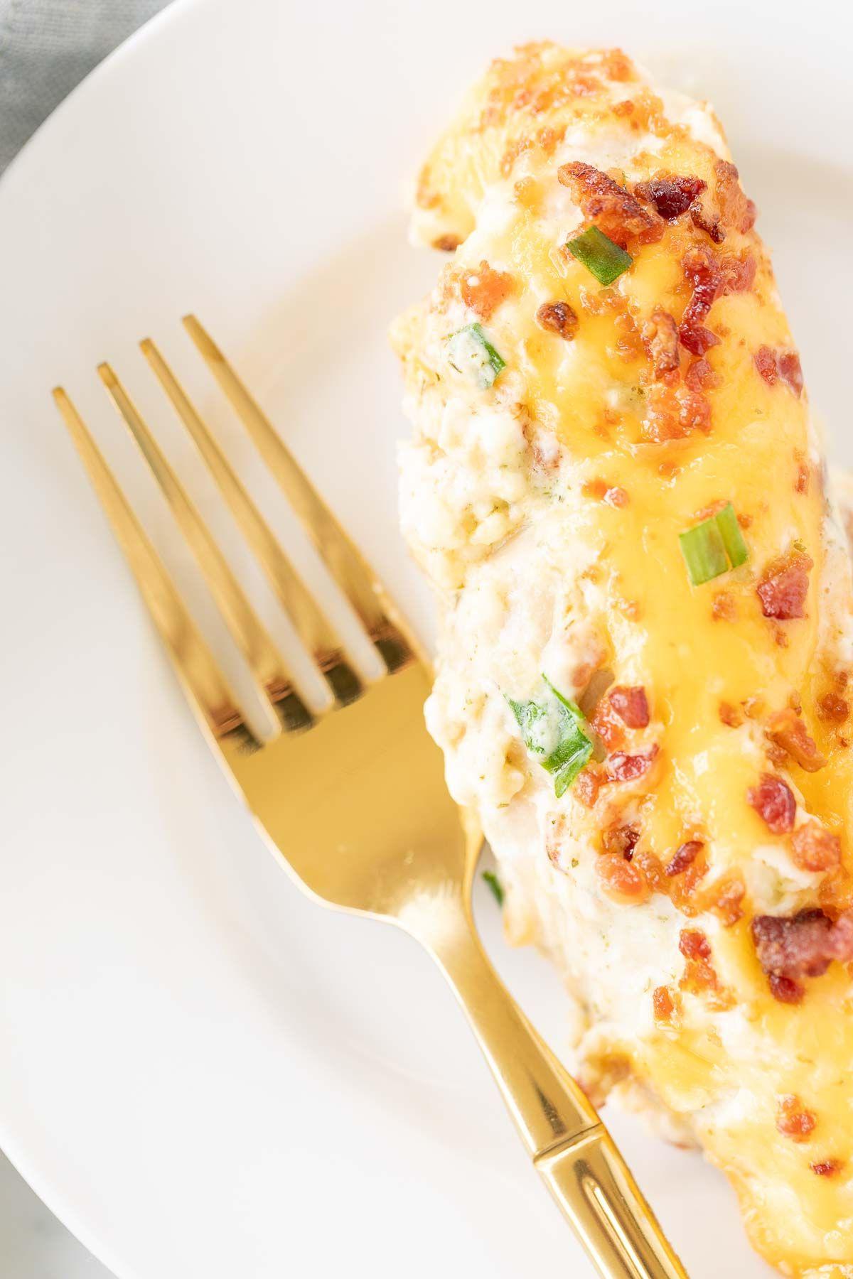 Nahaufnahme einer Portion Ranch 'Crack Chicken' auf einem weißen Teller, serviert mit einer goldenen Gabel.