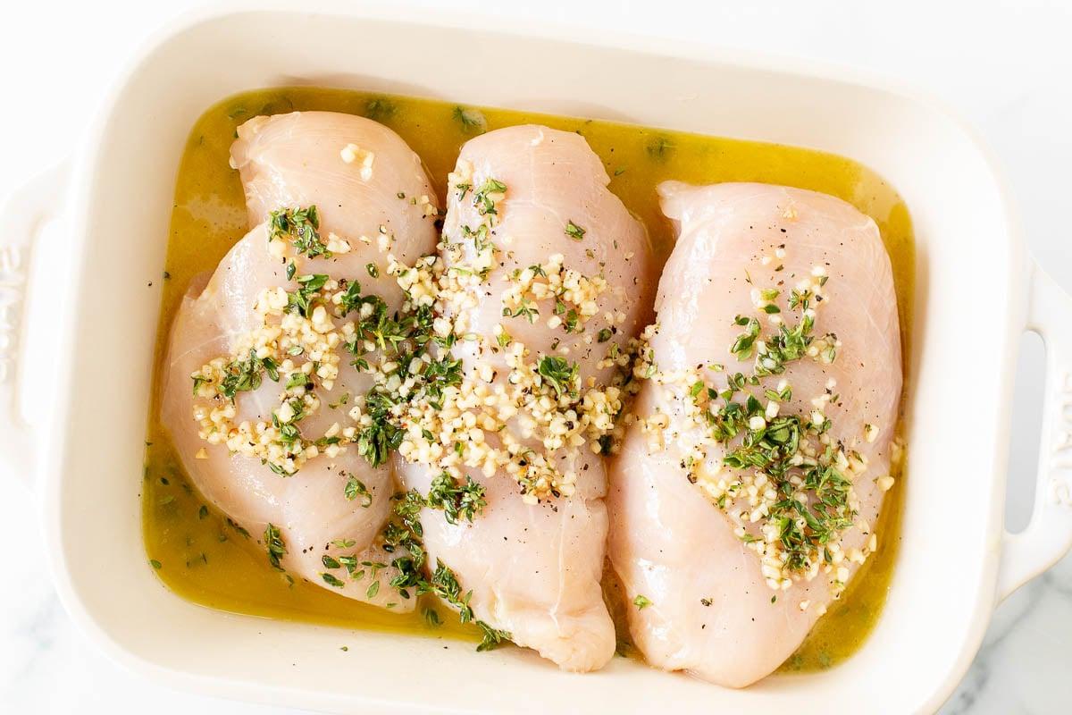 Marinierte griechische Hähnchenbrustfilets in einer weißen Backform.