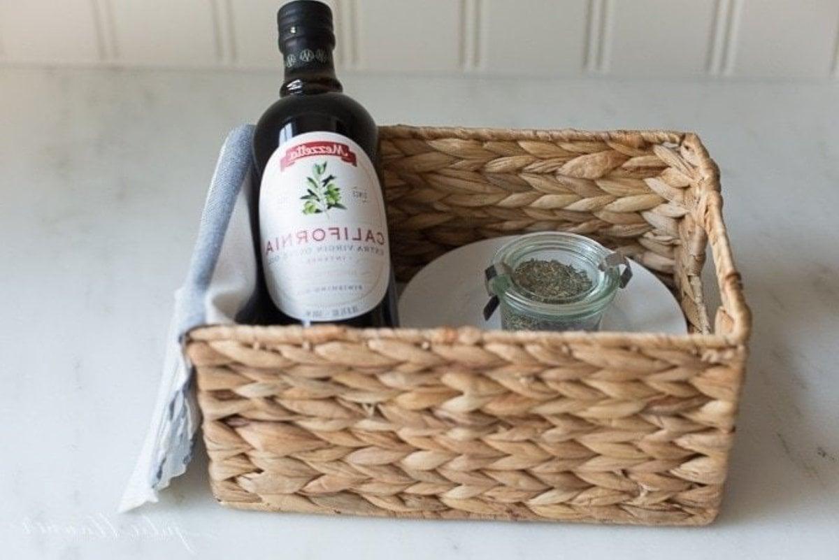 Olivenöl-Brot-Dip 16 Ein Geschenkkorb mit selbstgemachten Brot-Dip-Gewürzen, einem weißen Teller und einer Flasche Olivenöl.