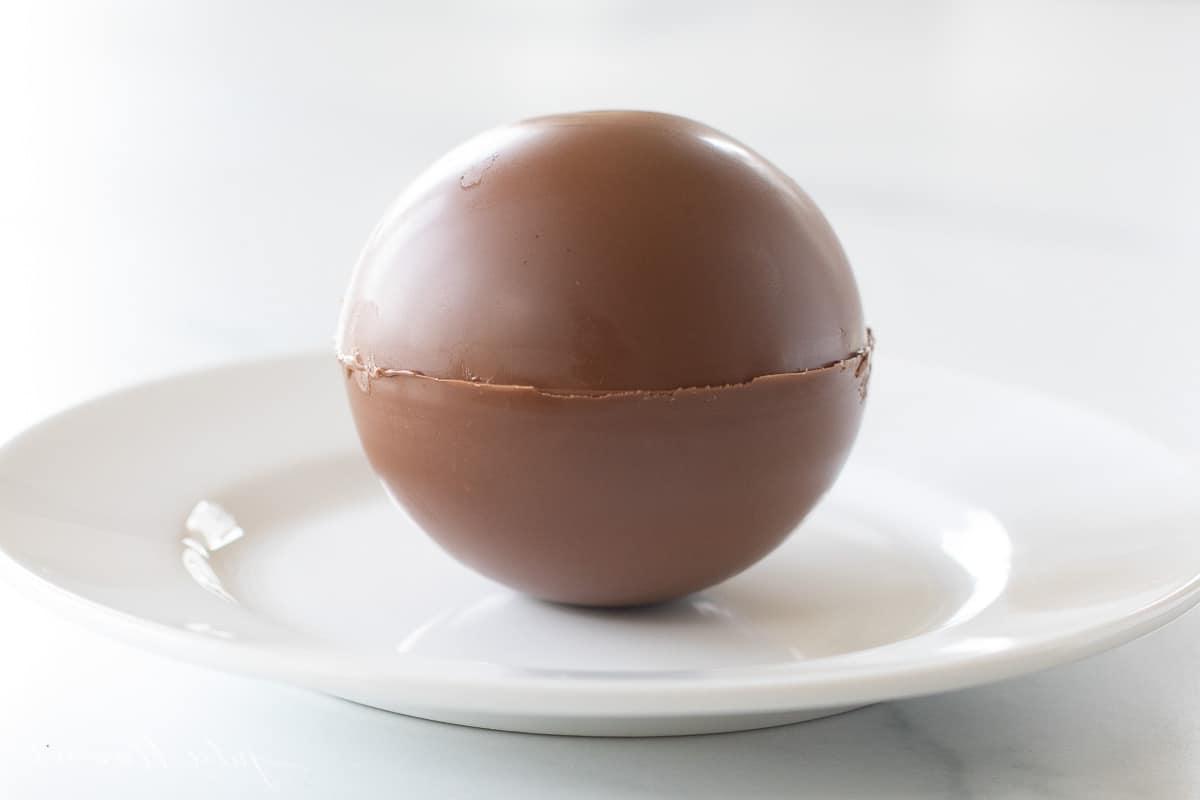 Ein weißer Teller mit einer einzelnen mexikanischen Trinkschokolade Bombe, beträufelt mit Cayennepfeffer und Schokolade, fertig dekoriert.