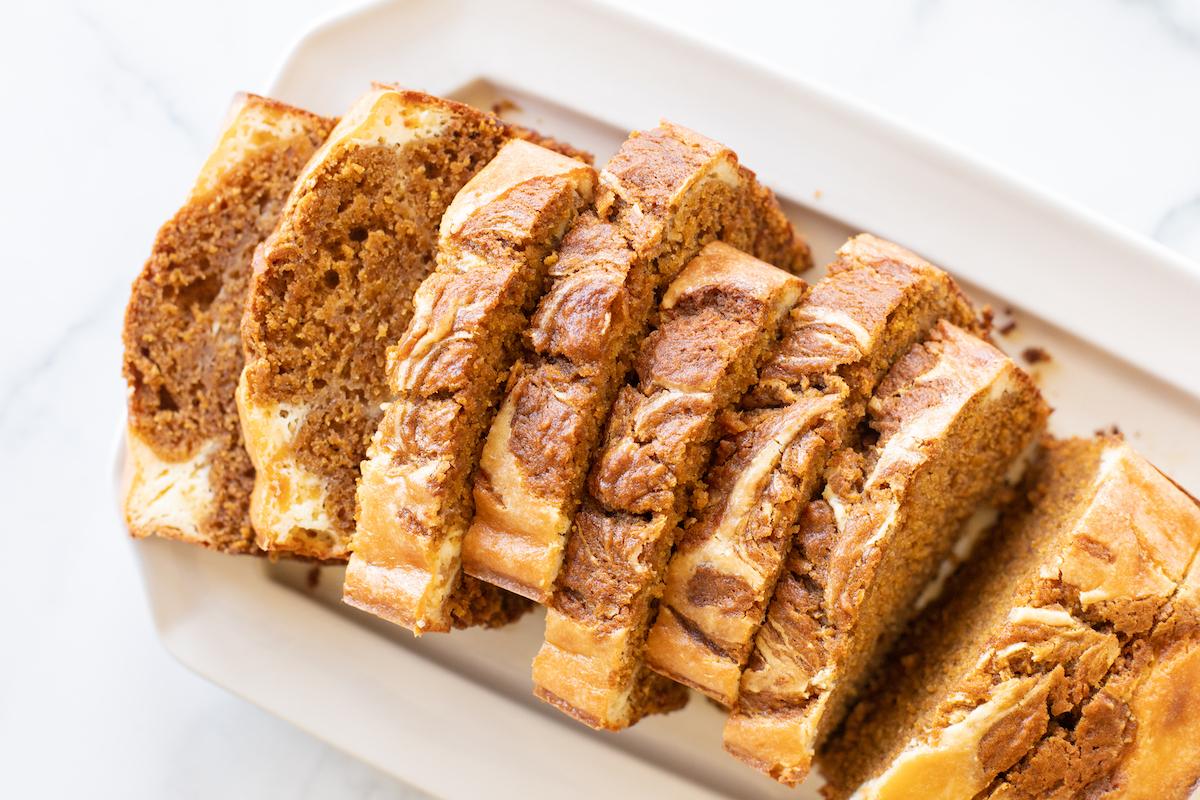 Ein frisch gebackener, goldbrauner Laib Kürbis-Käsekuchen-Brot, der auf einer weißen Platte präsentiert wird und sofort zum Anbeißen einlädt.
