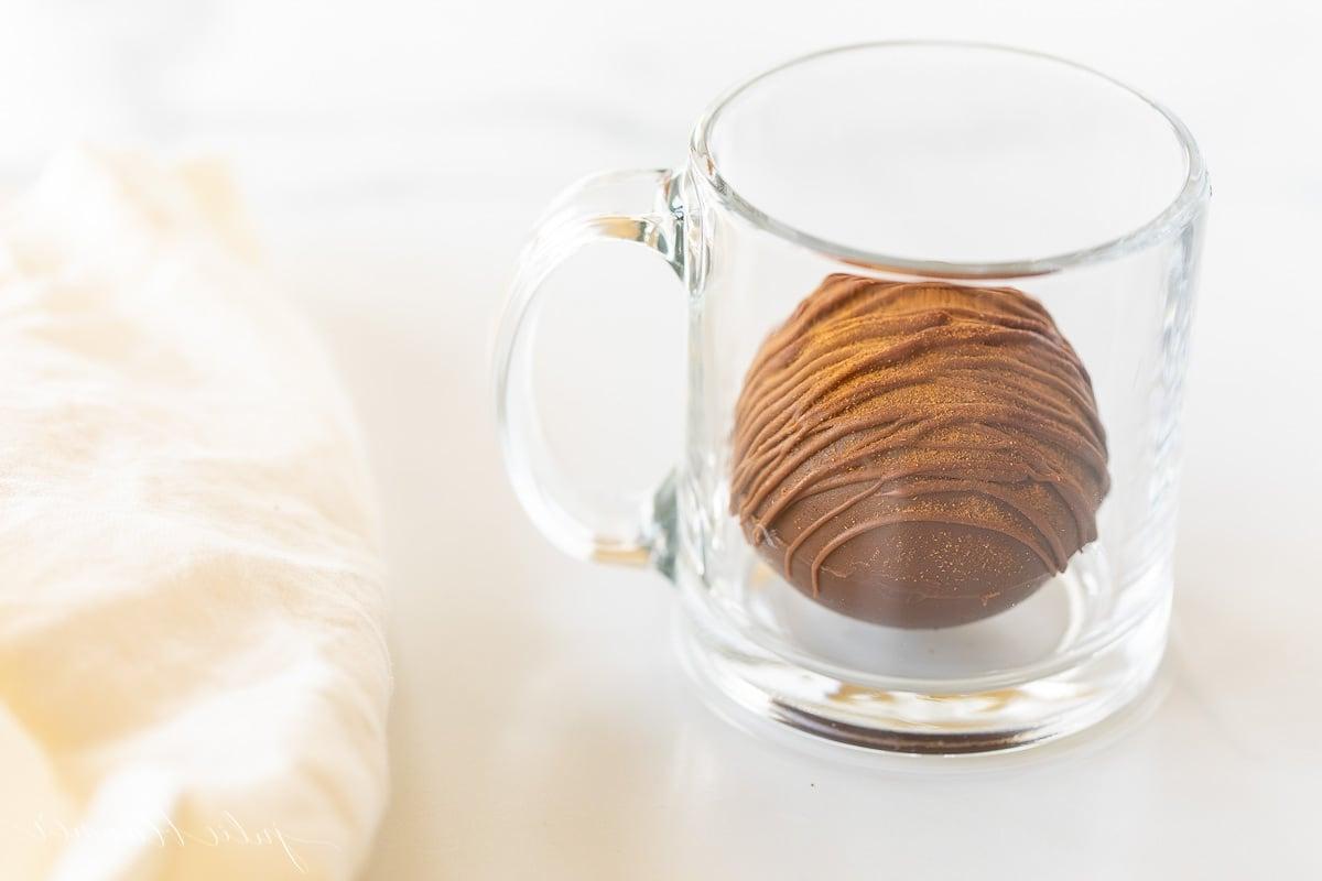 Mexikanische Heiße Schokoladenbomben 17 Eine klare Tasse mit einer würzigen Trinkschokolade Bombe, einem Zimtstiel und einer weißen Leinen Serviette daneben, bereit zum Genießen.