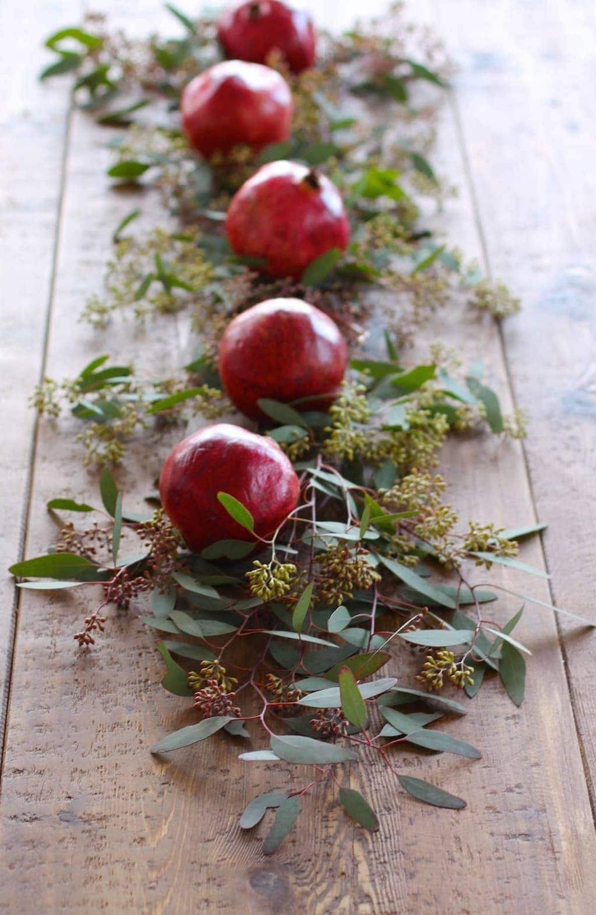 Granatapfel- und Eukalyptusblätter bilden ein atemberaubendes Weihnachts-Kerzen-Mittelstück auf einem Holztisch.