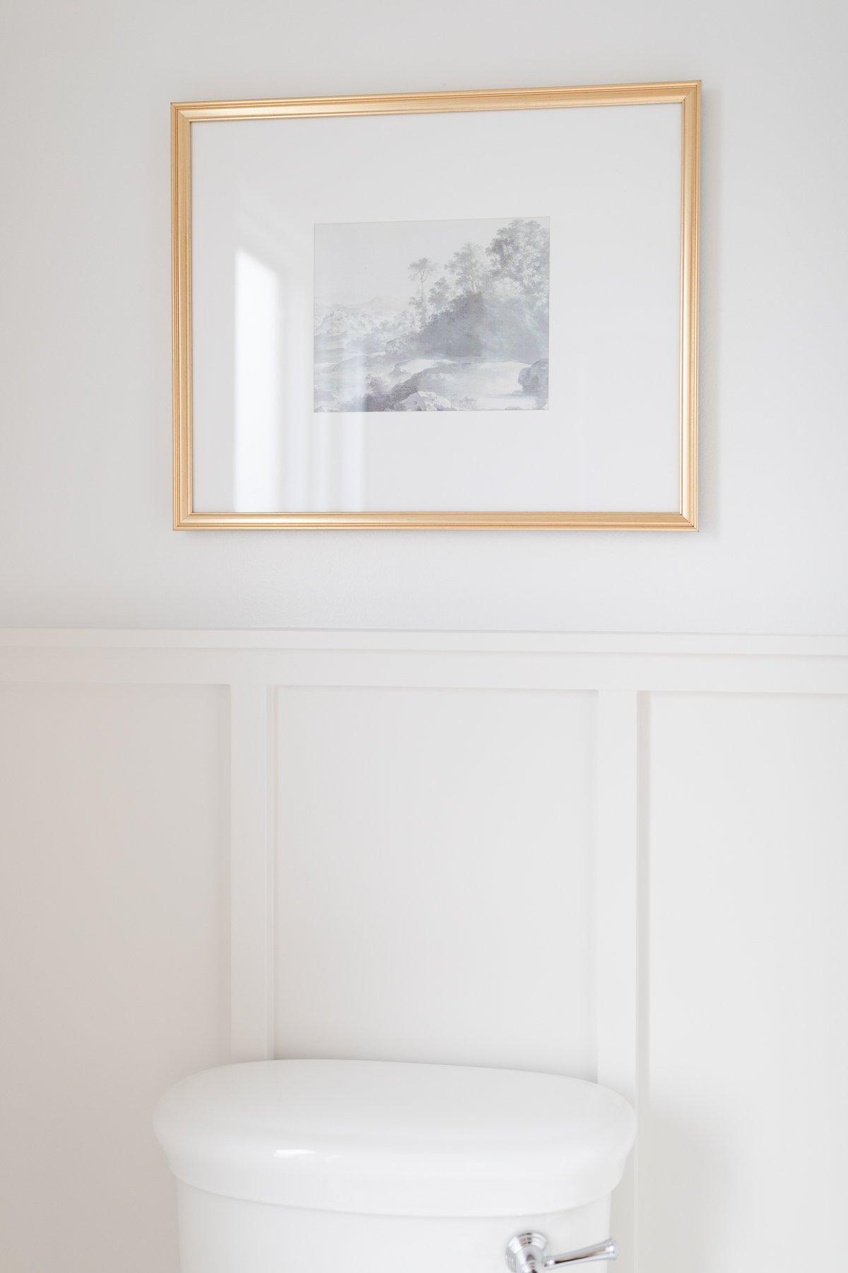 **Freie Kunstquellen** 20 Eine Toilette in einem weißen Badezimmer mit einem gerahmten Bild darüber, das von Studio McGee stammt und die ästhetische Integration von Kunst im Badezimmer zeigt.