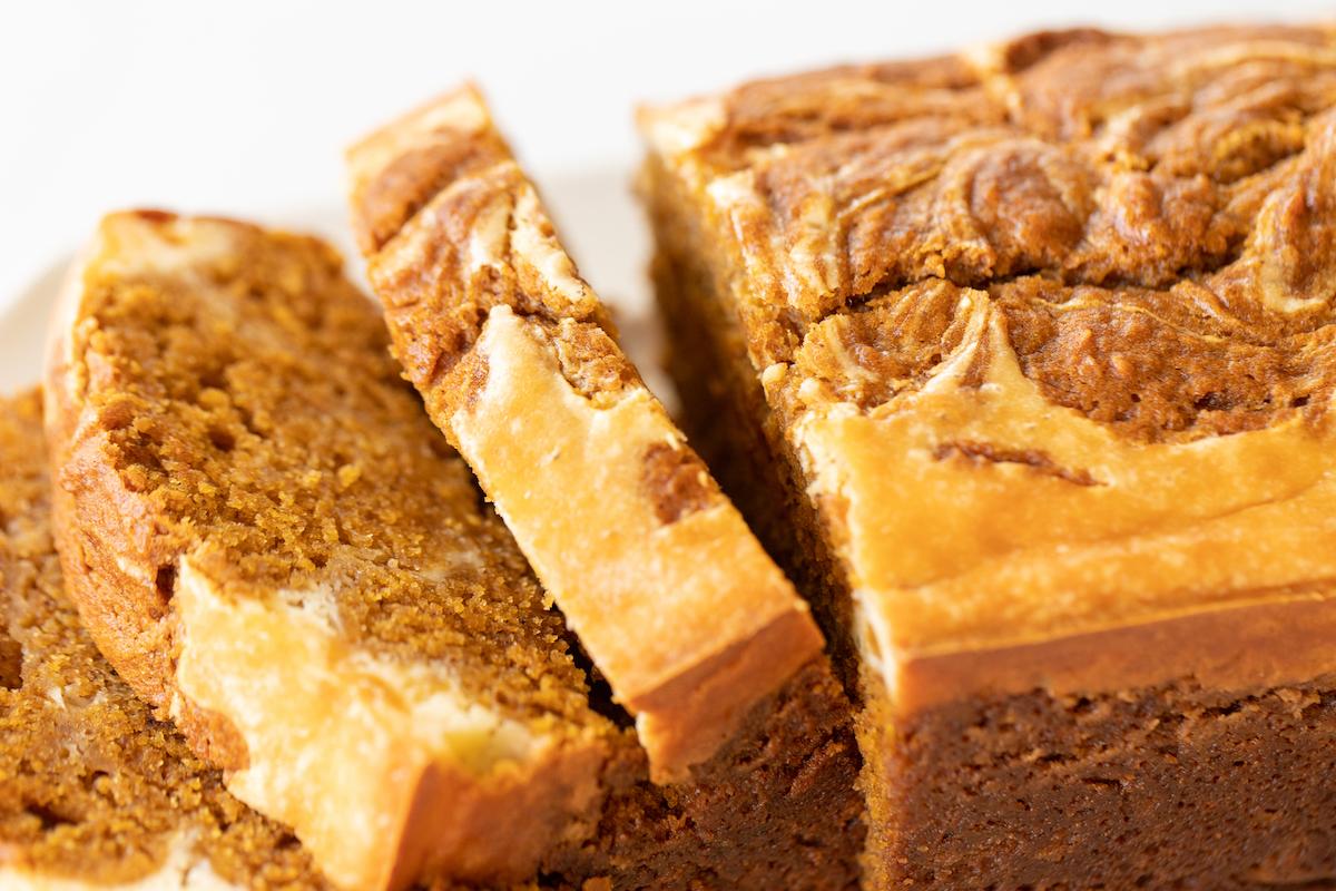 Ein ganzer Laib Kürbis-Käsekuchen-Brot, ansprechend auf einer weißen Platte präsentiert, mit Fokus auf die goldene Farbe und die leichte Kruste.