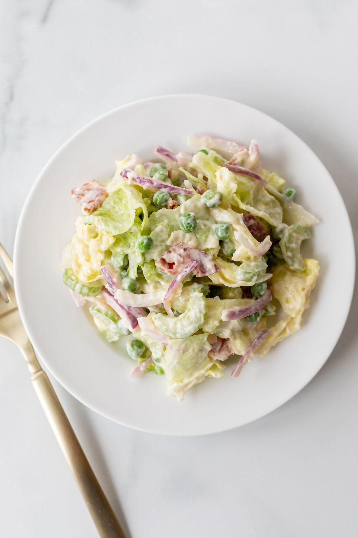 Siebenschichtsalat 20 Ein weißer Teller mit einer Portion Sieben-Schicht-Salat, Gabel daneben