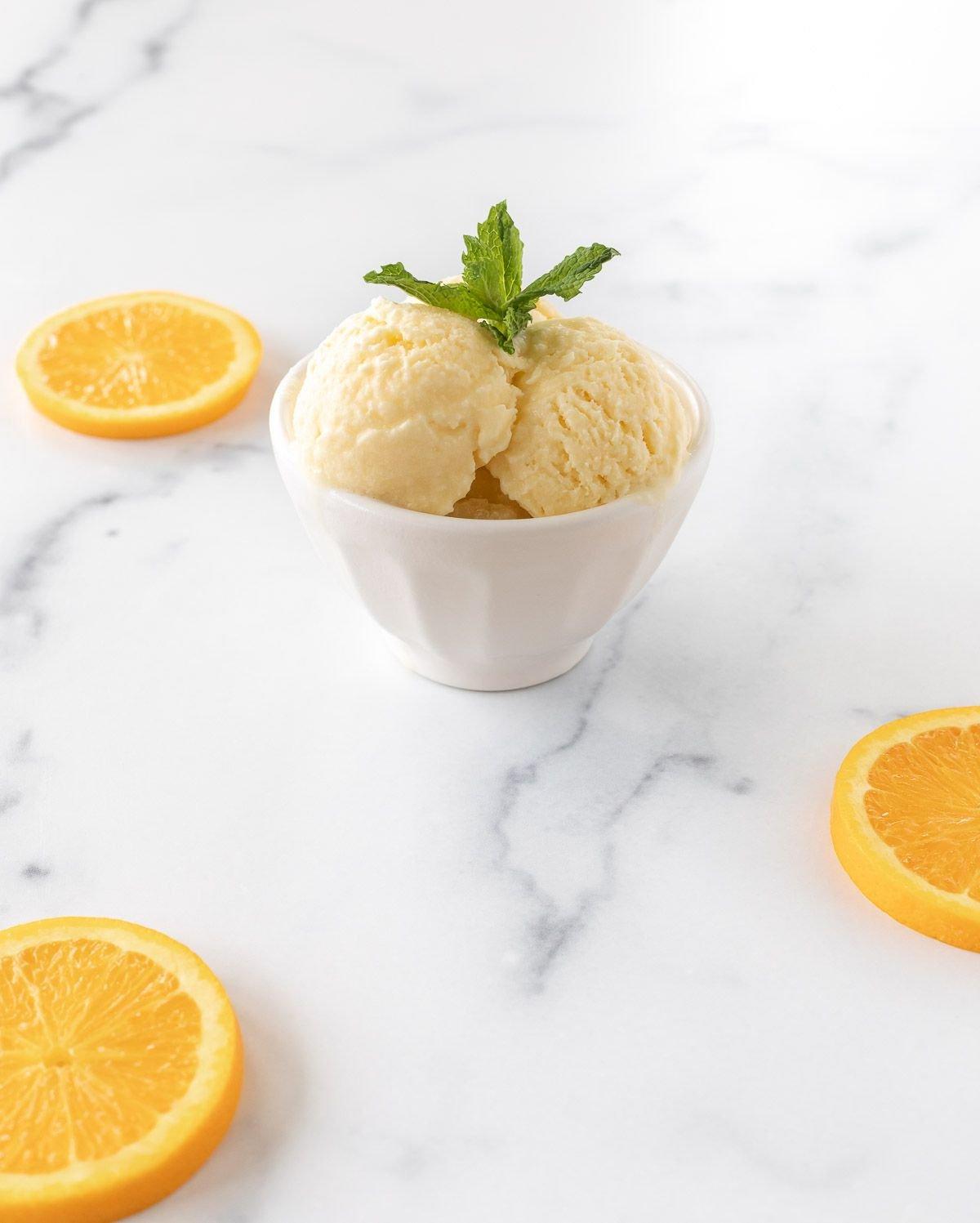 Orangen-Sorbet 3 Eine kleine weiße Schale voll mit Orangen-Sherbet auf einer weißen Oberfläche