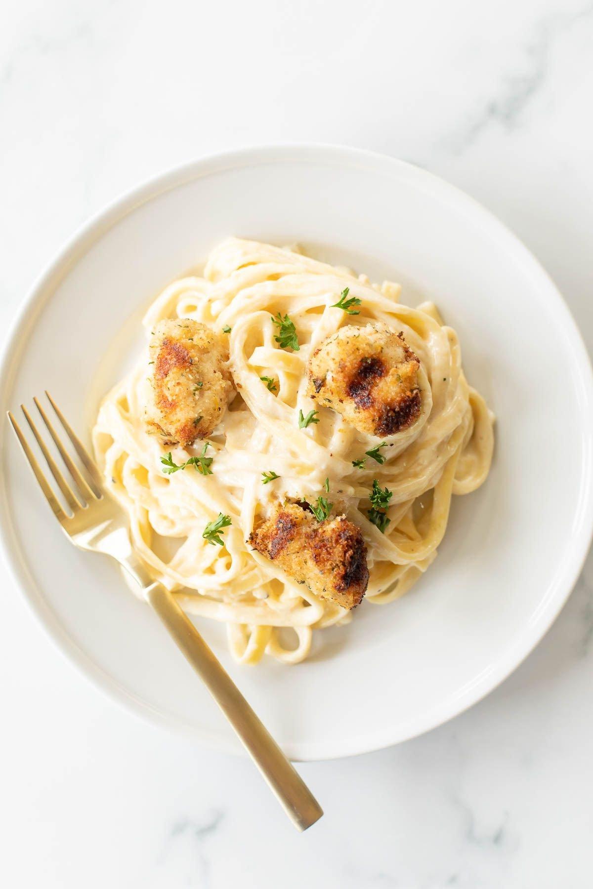 Spießchen 3 Ein weißer Teller mit Fettuccine Alfredo, garniert mit Spiedini.