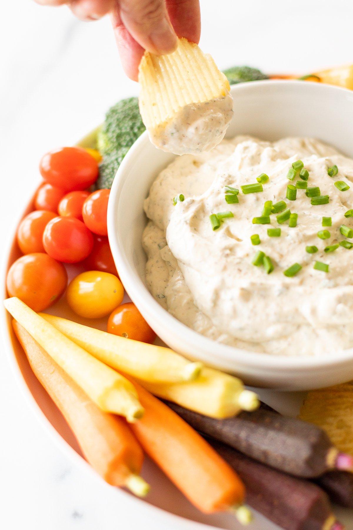 Ranch-Dip 3 Eine gerillte Kartoffelchips wird aus einem Ranch Dip in einer Schüssel auf einer Servierplatte mit Gemüse gehoben.