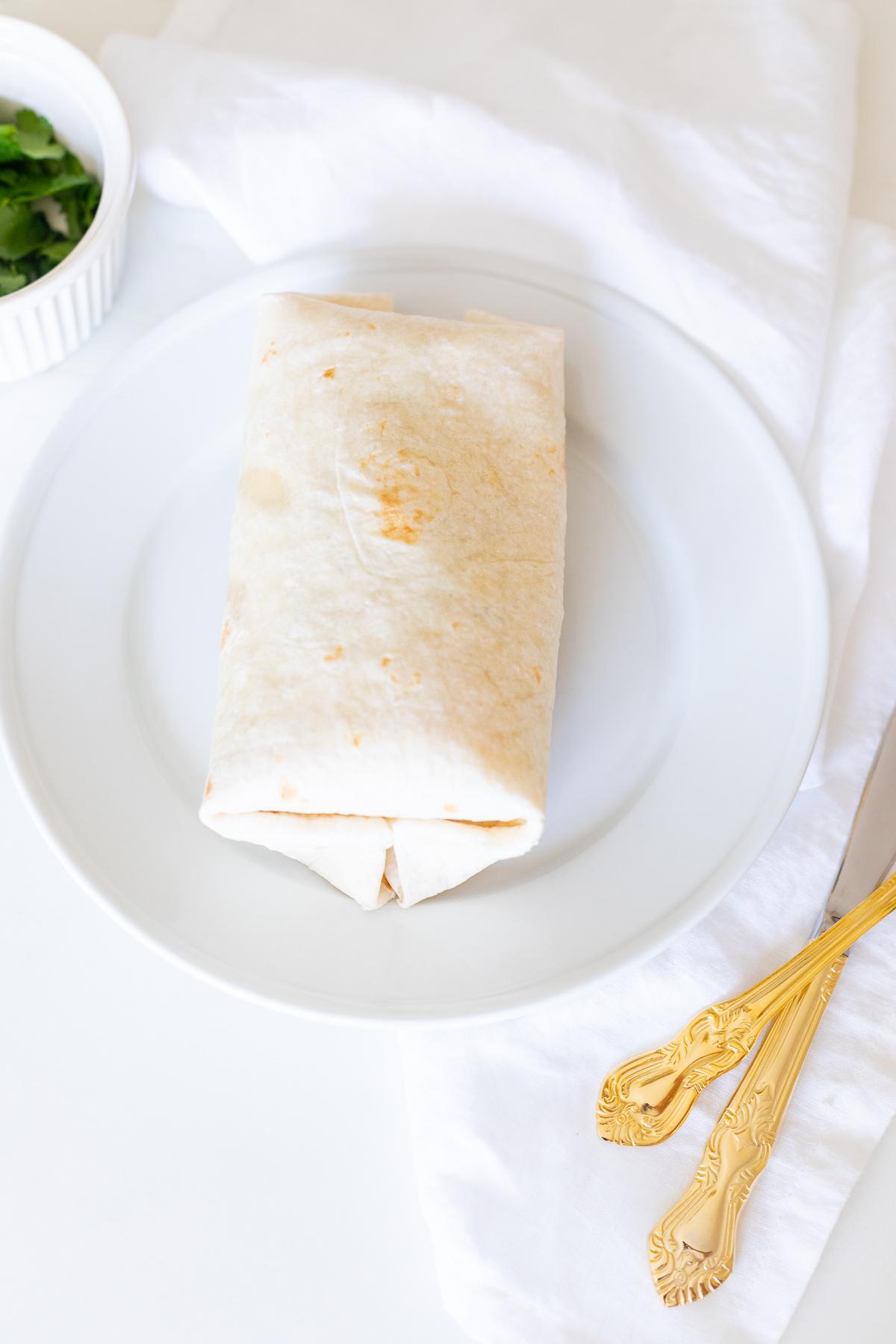 Hähnchen-Wrap-Rezept 3 Ein Hähnchen-Wrap auf einem weißen Teller mit goldenem Besteck.