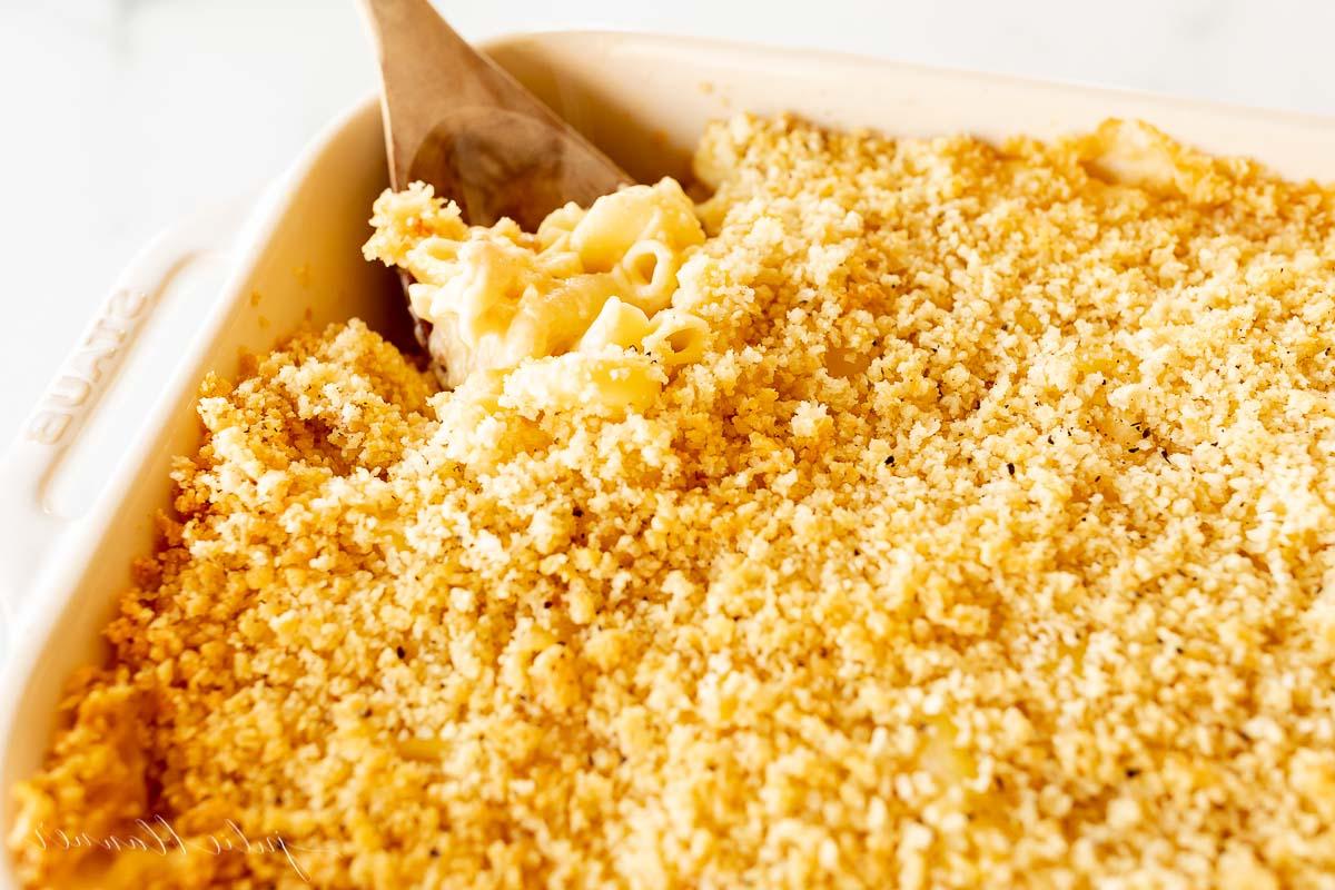 Speck Mac and Cheese in einer weißen Auflaufform mit einem Holzlöffel.